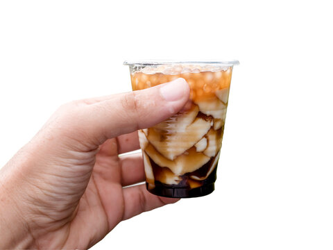 A hand holding a plastic cup of taho on a white background. Taho is a Philippine snack made of soft tofu, carmelized sugar and sago pearls.