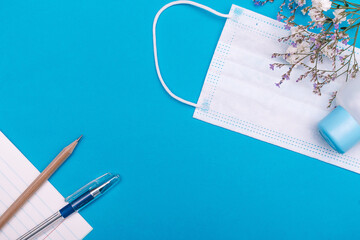 School stationery supplies,flowers, protective face mask and hand sanitizer antiseptic on blue...
