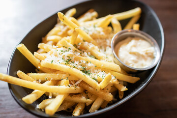 Cheese and parsley french fries in black bowl on wooden table.