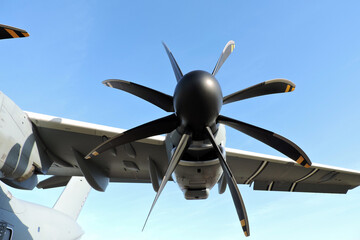 A close-up of a propeller with eight blades and a wing of a military transport aircraft