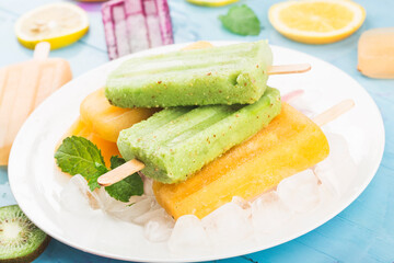 Various fruit popsicles are placed on the blue wooden board background, kiwi popsicles, orange popsicles, dragon fruit popsicles, cantaloupe popsicle
