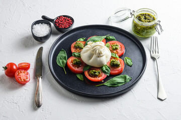 burrata Buffalo  cheese served with fresh tomatoes and basil leaves pesto sauce on black plate white background