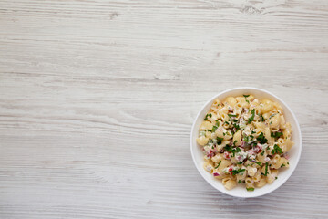 Homemade Macaroni Salad in a white bowl on a white wooden background, top view. Flat lay, overhead, from above. Space for text.