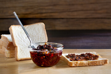 Chili paste smear on front of bread for eat, and pile of breads on brown wooden chopping board on...