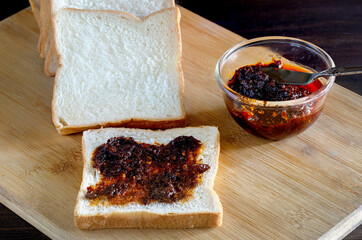 Chili paste smear on front of bread for eat, and pile of breads on brown wooden chopping board on...