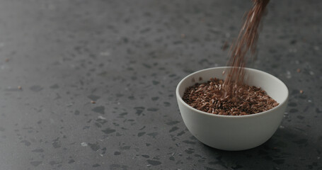 flaxseed falling into white bowl on terrazzo countertop