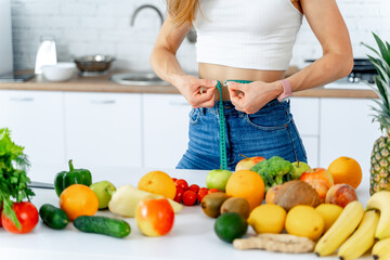 Measuring tape around waist. Woman in kitchen. Healthy food and dieting.