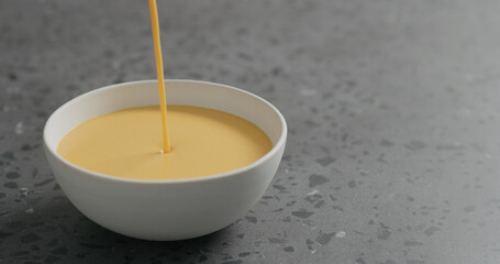 pour pumpkin cream soup in white bowl on terrazzo countertop