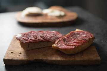 Ciabatta slices with slices of salami sausage on olive wood board