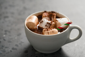 Cocoa drink with marshmallow and christmas drinking straw in white cup on terrazzo surface with copy space