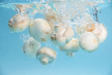 Appetizing mushrooms are falling into clean transparent water, forming lots of splashes. Concept of fresh tasty products