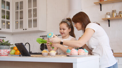 Young mother and little daughter icing cupcakes 