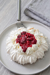 Raspberry pavlova with cake slicer on a grey plate.  Grey wood background