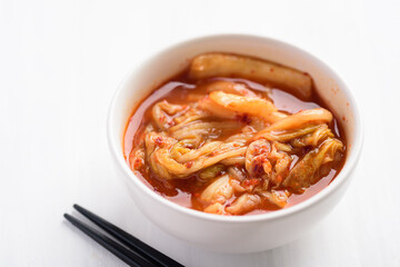 Kimchi cabbage in a bowl with chopsticks on white table, Korean food