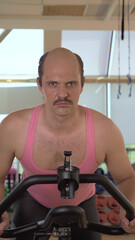 vertical, medium shot, funny bald man is training on an exercise bike, smiling