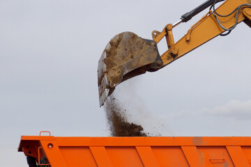 Loading soil into the back of a truck with a large excavator bucket.