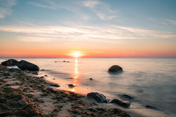 Long exposure of sunset over the ocean with beautiful beach and rocks in the forground