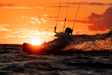 Silhouette of kitesurfer riding in beautiful orange sunset with the sun right behind - obrazy, fototapety, plakaty