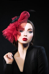 Young woman fashion portrait, red hat, evening make-up, black toxedo wear. Dark background