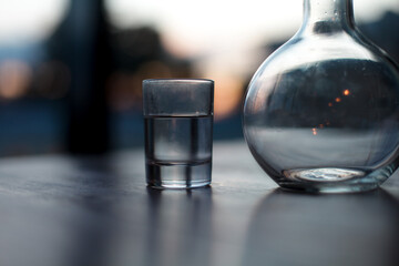 a glass of vodka next to a glass decanter in the sunset light and the light of lanterns