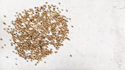 Unpeeled cannabis seeds on white stone like board, view from above - space for text right side