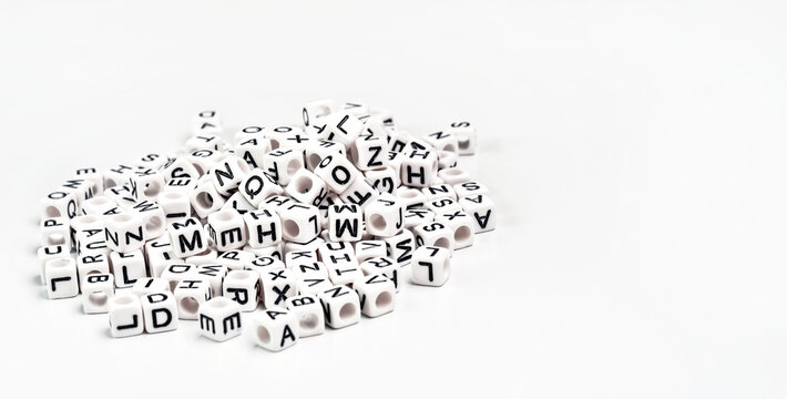 Heap Of Small White Cube Beads With Various Letters Scattered On Board, Space For Text Right Side