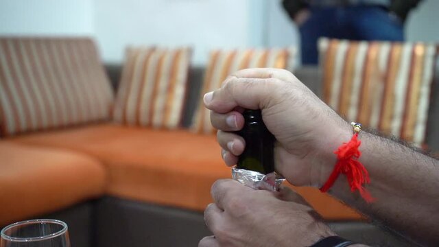 Man with a rakhi popping open the cork of a bottle of champagne in slow motion with vapor coming out