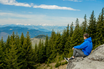 A tourist sits on cliff and looks into the distance. Man sit. Wonderful mountain landscape. Summer is time