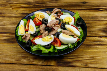 Tasty tuna salad with lettuce, black olives, eggs and fresh vegetables on wooden table