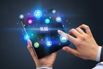 Businessman holding a foldable smartphone with VLOG inscription, social media concept