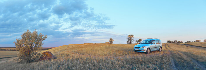 A blue car stands on a hill next to a country road, the concept of car travel. Panorama, selective focus.