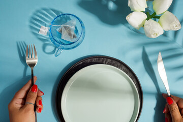Dinner table with ceramic plate and woman hand holding knife and fork.