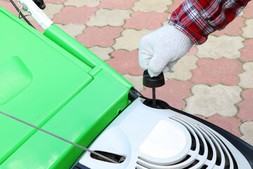 Male Checking the oil level in lawn mower. A green lawnmower. Gardening. Maintenance of equipment.