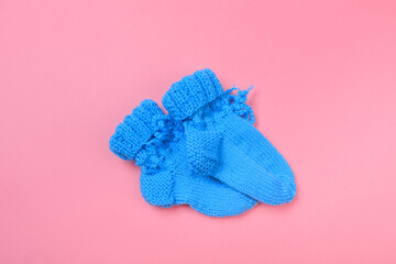 knitted baby booties on pastel pink background.