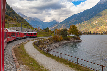 Beautiful view of  red  Rhaetian train running on the lake side of Lago di Poschiavo in autumn with...