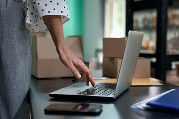 Taking orders online. Cropped shot of a woman, female business owner using laptop while standing in her shop or store