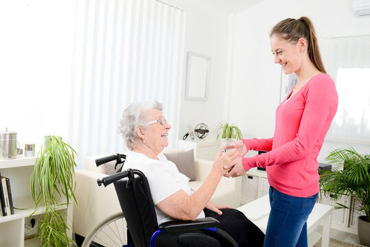 cheerful young woman taking care at home of elderly woman on wheelchair