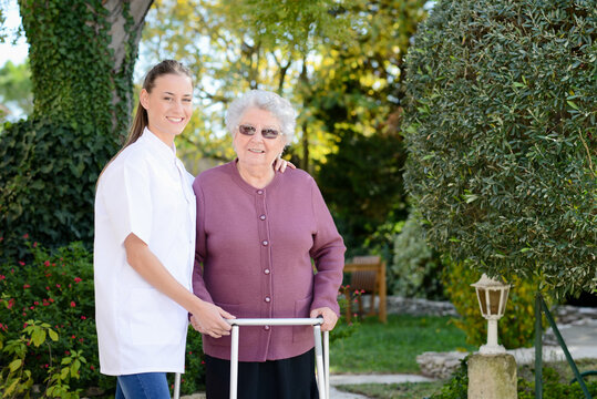 Elderly senior woman with a nurse walking outdoor in nursing home hospital garden