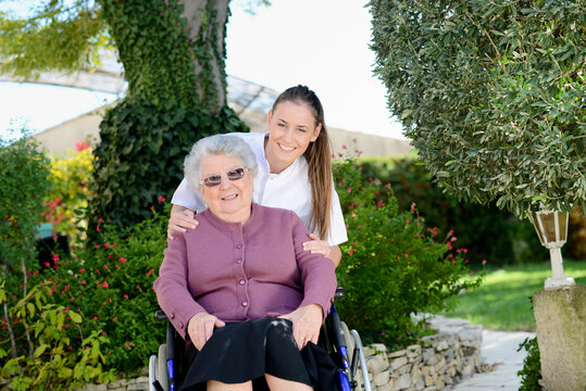 Elderly senior woman on wheelchair with a nurse outdoor in nursing home hospital garden.