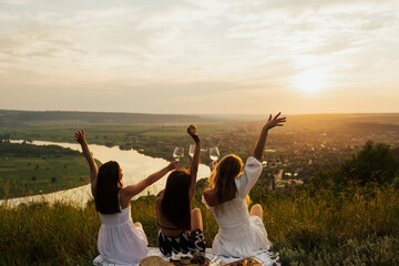 Three best girlfriends having fun together on a picnic on the mountain at sunset. They enjoying...