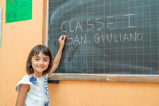 Young girl on her first day of elementary school in the classroom writing on the chalkboard