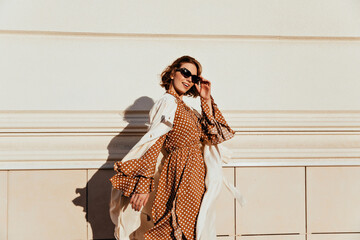 Pretty woman in long brown dress enjoying sunny day. Lovable white girl in retro attire walking...