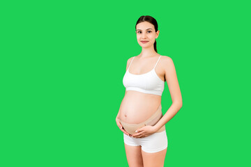 Portrait of supporting bandage on pregnant woman in underwear at green background with copy space. Orthopedic abdominal support belt concept