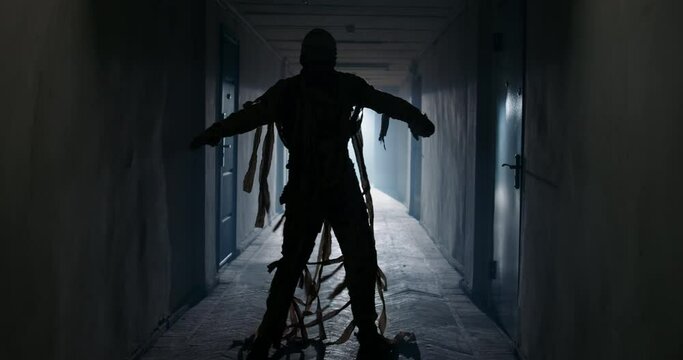 Guy in thematic bandaged costume of halloween mummy doing a funny dance in corridor, celebrating halloween - horror, halloween concept 4k footage