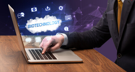 Businessman working on laptop with BIOTECHNOLOGY inscription, modern technology concept