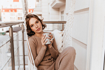 Beautiful girl in knitted dress drinking coffee in morning. Romantic caucasian young woman holding...