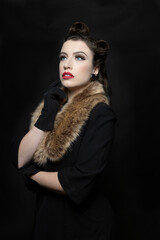 A 1940's woman wearing a black coat, fur collar, and a hat with a veil.  