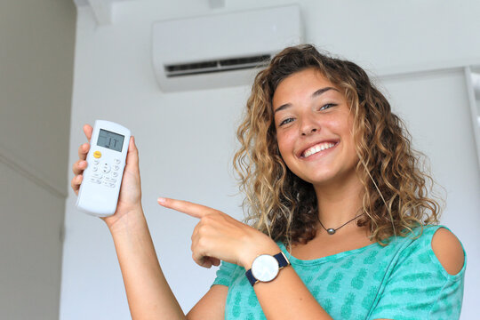 Young woman using a remote control of wall-mounted air conditioner.