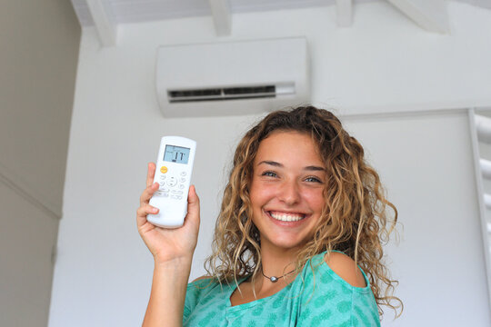 Young woman using a remote control of wall-mounted air conditioner.