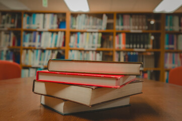 Stack of books on table and blurred bookshelf in the library room, education background.